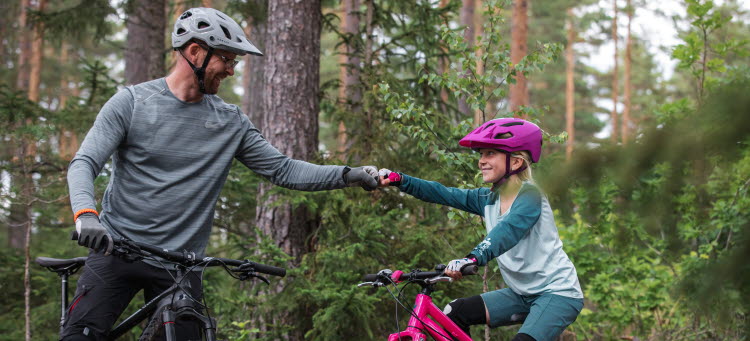 Vuxen och barn stigscyklar tillsammans i skogen.