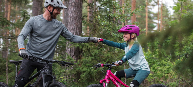 Barn och vuxen cyklar i skogen och gör en så kallad "fistbump".