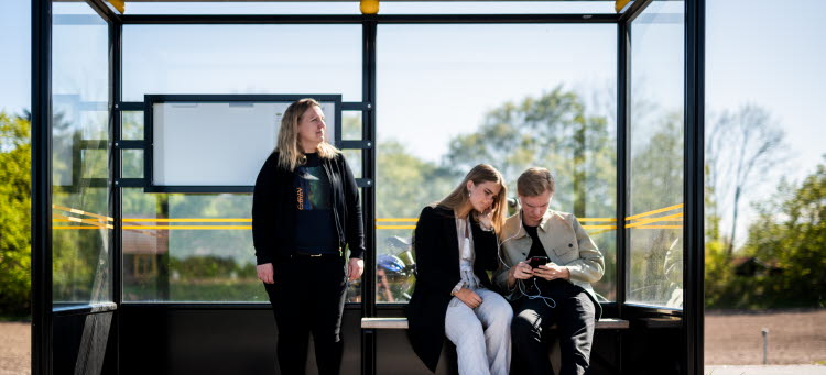 Bild på busshållplats med tre personer.