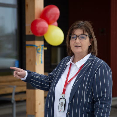 Tina Gardelin byggprojektledare står utanför Högsby hälsocentral där röda och gula ballonger hänger i bakgrunden.
