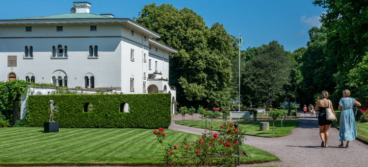 Två kvinnor går i solskenet med ryggen mot kameran på grusvägen framför Sollidens slott.
