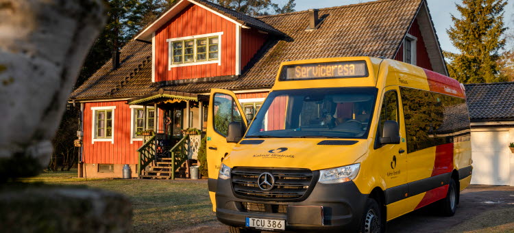 En färdtjänstbuss står parkerad med passagerardörren öppen framför en röd villa.