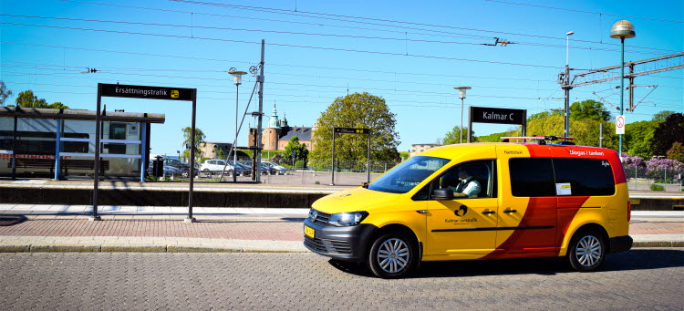 Gul och röd färdtjänstbil i stationsmiljö.