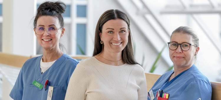 tre medarbetare står i en korridor och tittar in i kameran