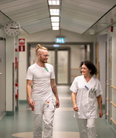 Två medarbetare i vårdkläder tittar på varandra och ler.