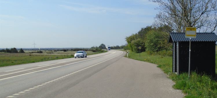 Landsväg med en bil och en busshållplats till höger. 