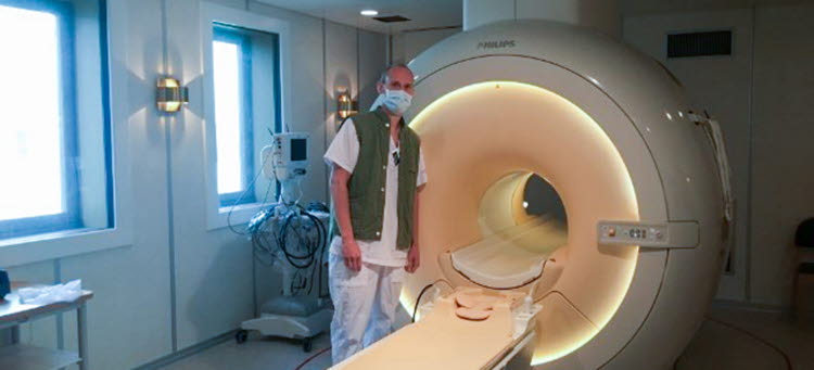 Man som står framför en röntgenmaskin, han är vårdklädd och bär munskydd. 