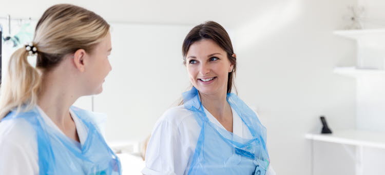 Två vårdklädda medarbetare tittar på varandra och ler