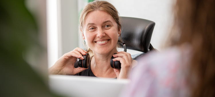 En person är på väg att sätta på sig headset och ler snett in mot kameran.
