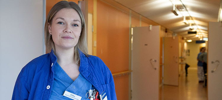 en vårdklädd person står i en korridor och tittar in i kameran